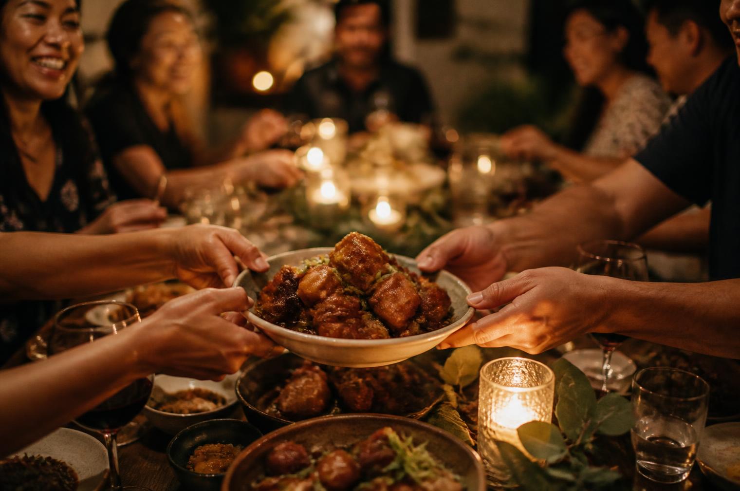 Friends passing a shared bowl of food across a candlelit table